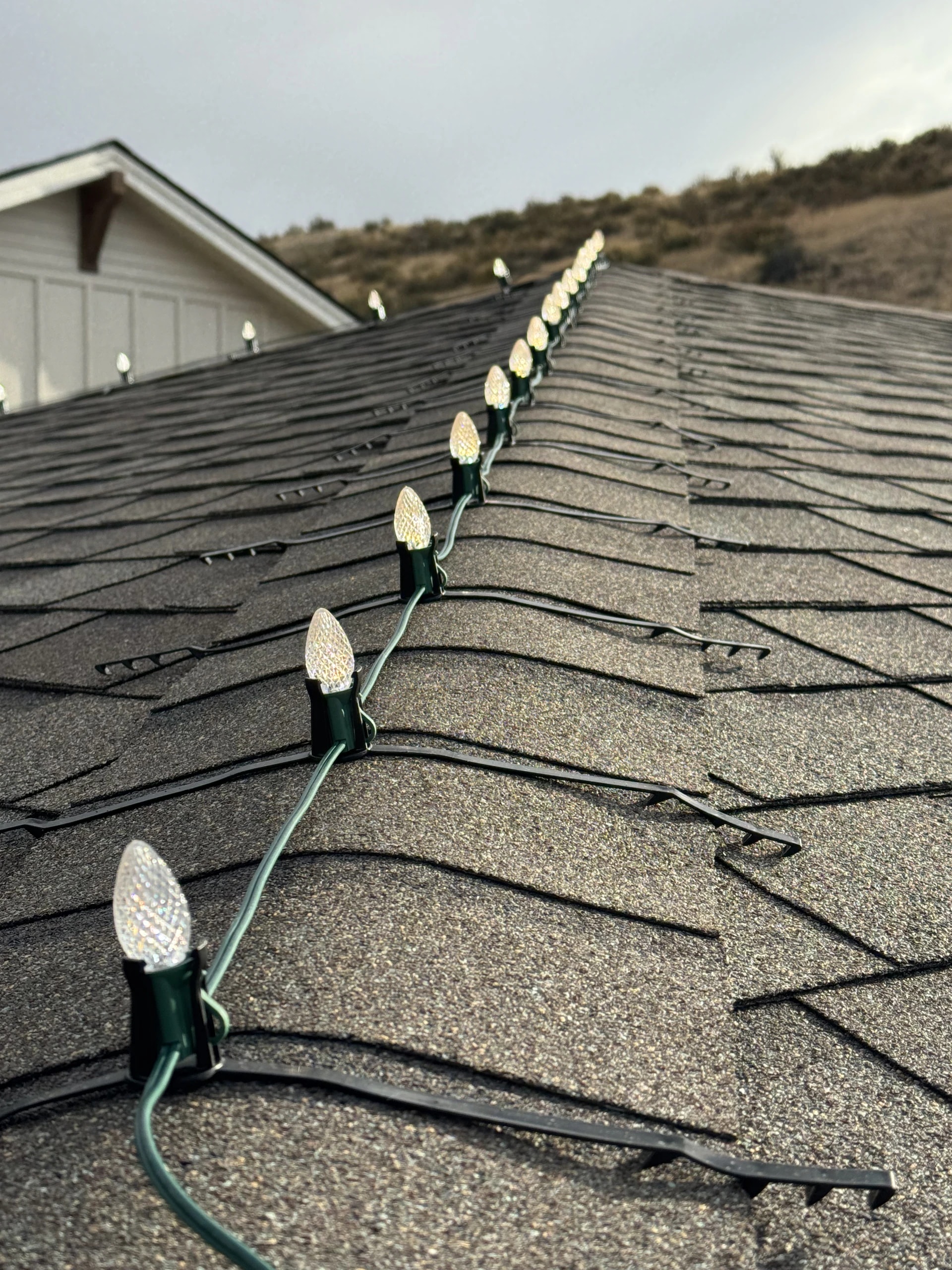 Close-up of C9 Christmas lights clipped to an asphalt shingle roof in Boise, ID by Christmas Light Installation Boise